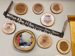 This image features an old fashioned tree saw and several recognition trophies from Hancock Lumber on slices of logs.  There is also a mirror in a log frame.